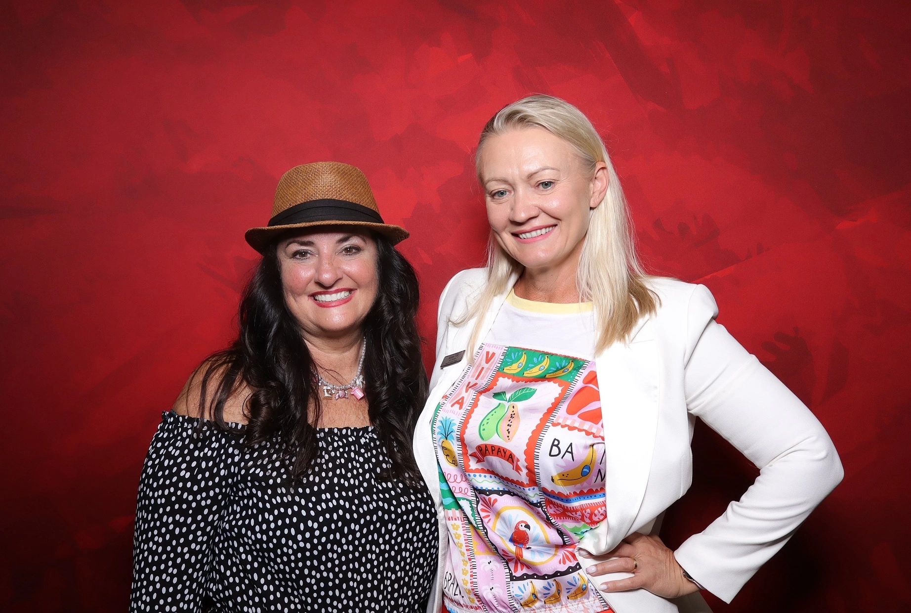 Two women smiling against a vibrant red background.