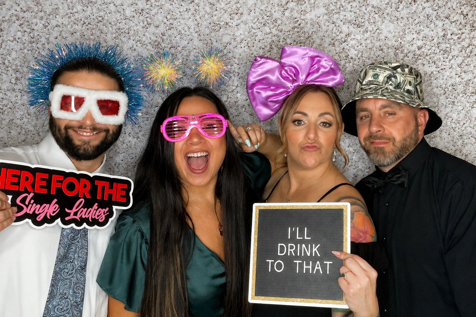Four friends wear fun accessories and hold signs at a lively party photo booth.