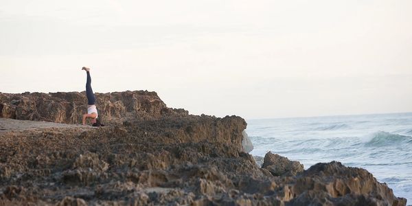 A woman doing a headstand at the ocean.