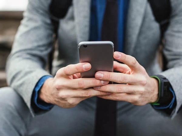 Man in suit holding smartphone, sitting on steps.
