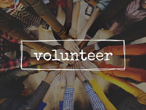 Diverse group joining hands in unity with the word 'volunteer' overlay.