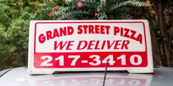 A sign board of grand street pizza on the car