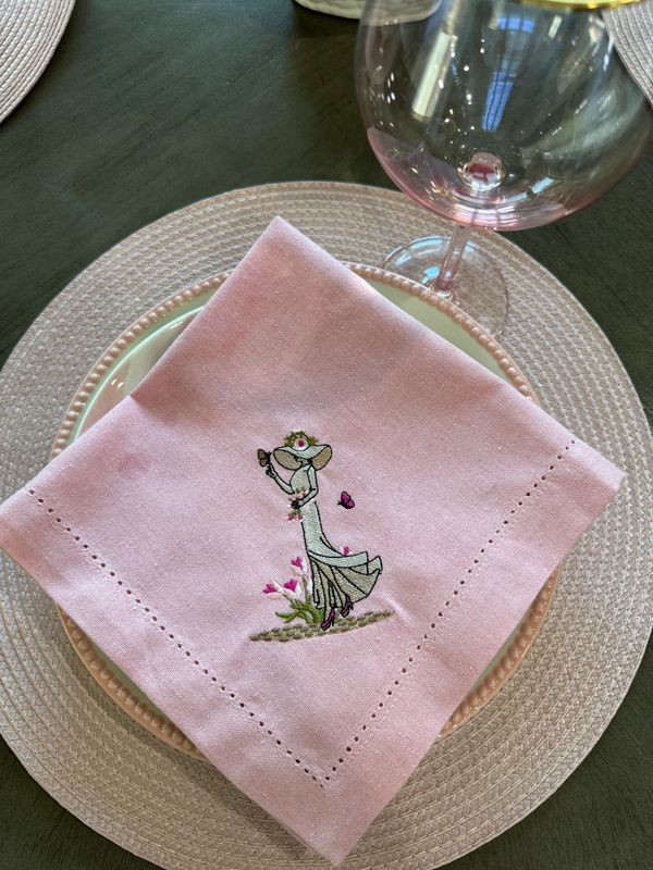 Pink embroidered napkin on a decorative plate with a wine glass.