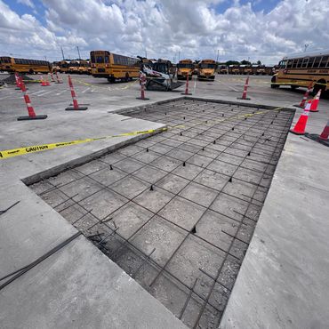 Construction site with school buses and concrete reinforcement work under cloudy sky.