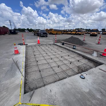 Construction site with rebar grid for concrete slab and school buses in background.