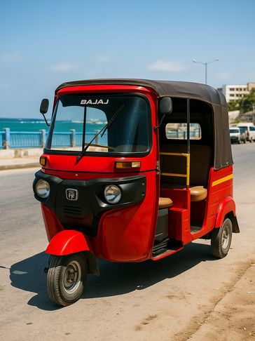 A red Bajaj auto rickshaw parked by the seaside under a clear blue sky.