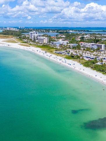 Aerial view of a sunny beach with turquoise water and beachfront buildings.