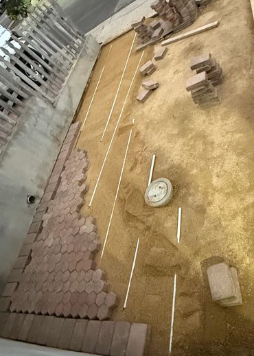Ongoing outdoor paving project with hexagonal bricks and white spacers on sand.