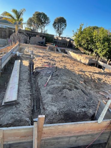 Construction site with foundation trenches and wooden formwork under clear sky.
