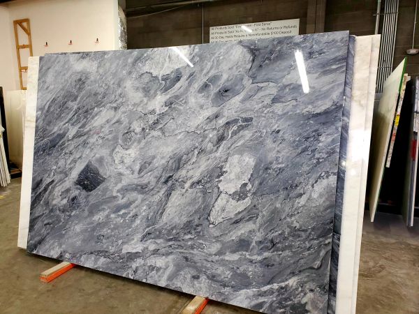 Large polished slab of blue-gray marble with swirling patterns, standing in a warehouse.