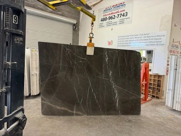 Large dark marble slab suspended by a crane inside a warehouse.