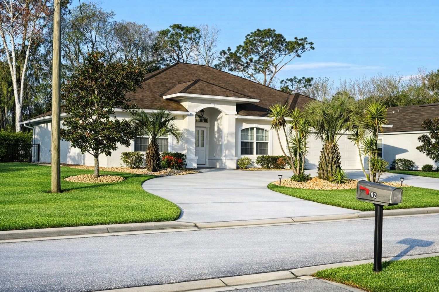 Single-story suburban house with a curved driveway and lush landscaping.