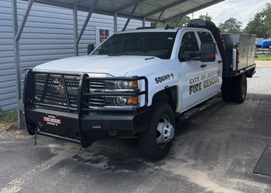 White fire rescue truck labeled 'Squad 3' parked under a metal carport.