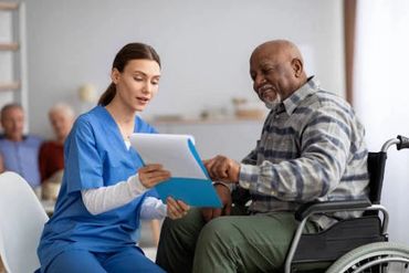 Nurse discussing documents with elderly man in wheelchair.