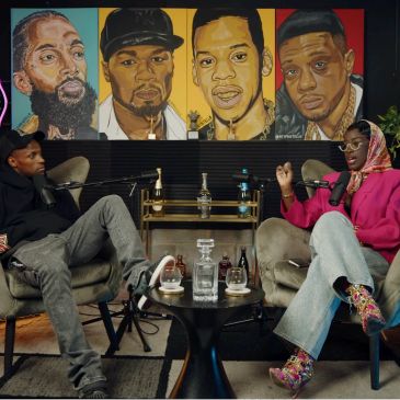 Two people recording a podcast in a stylish room with portraits of hip-hop artists.