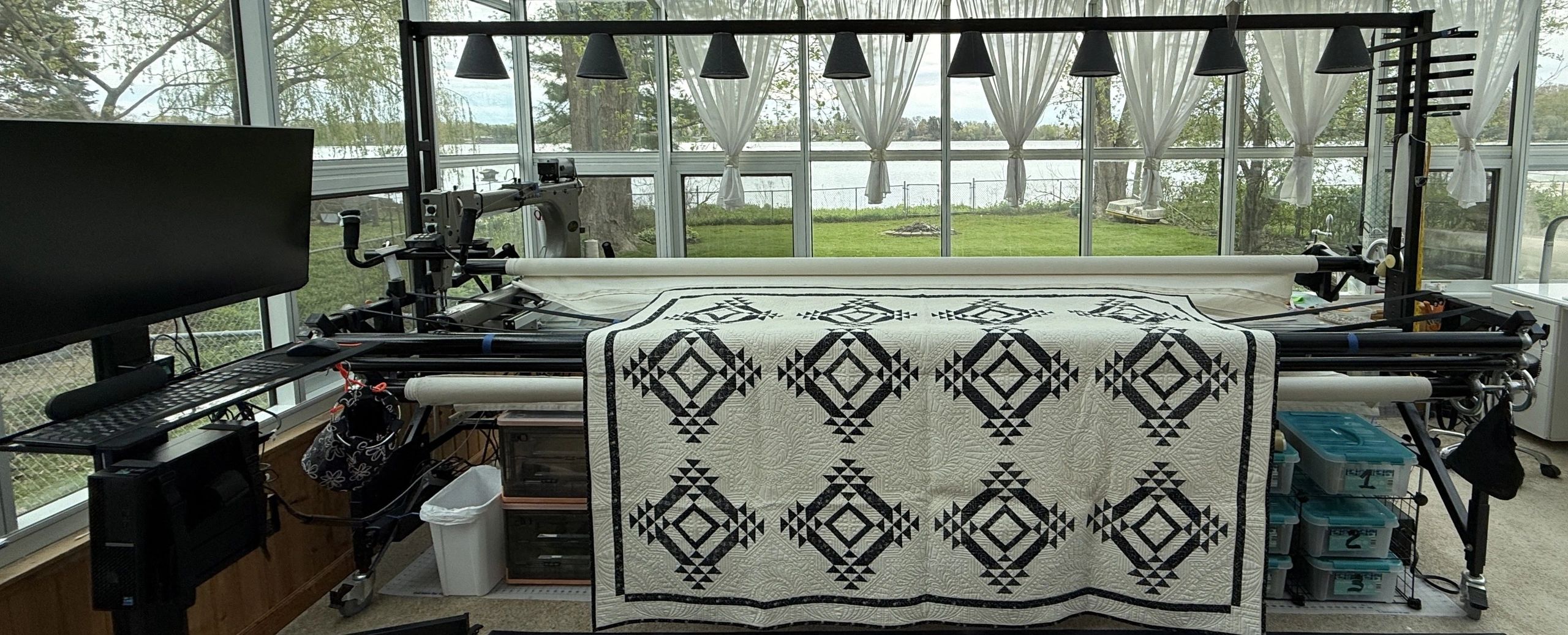A longarm quilting machine stitches a black and white geometric quilt