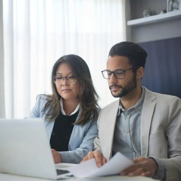Two professionals reviewing documents together at a laptop.