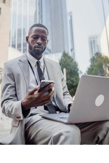 Man in a suit using phone and laptop outdoors in a city.