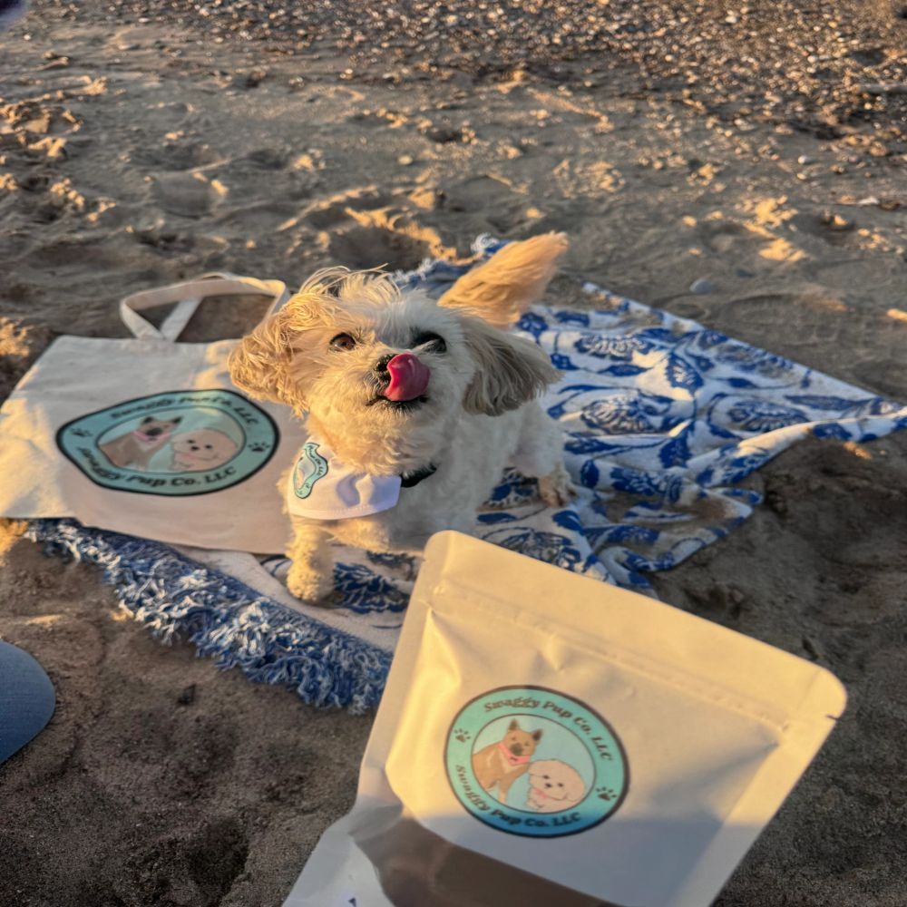 Small dog licking nose on beach blanket with branded products.