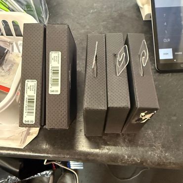 Stacked black boxes with price tags on a counter beside a tablet.