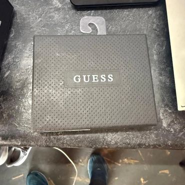 A textured Guess brand box on a countertop with blue shoes visible below.
