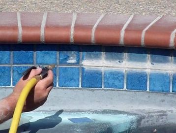 Person cleaning a tiled pool edge with a hose.
