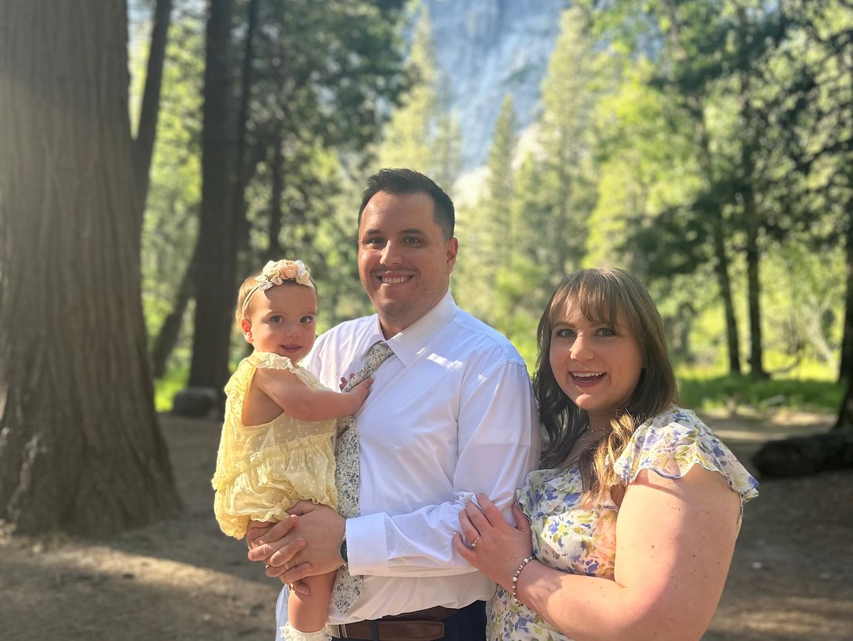 A happy family of three posing outdoors in a sunny forest.