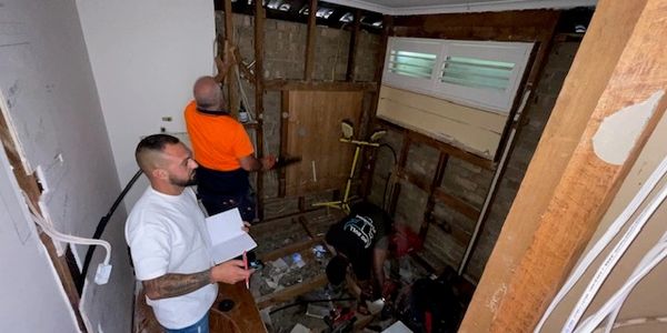 Three men renovating a room with exposed walls.