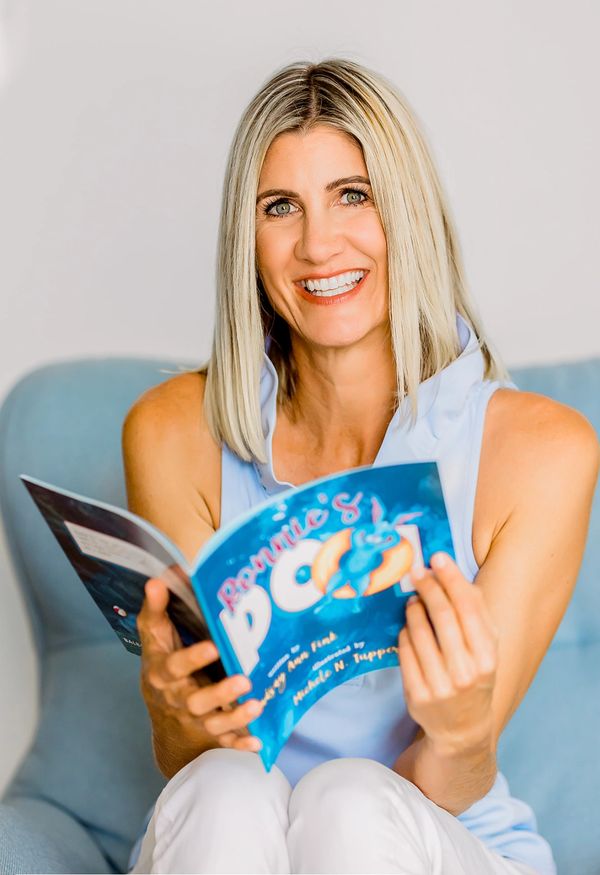 Woman smiling and reading a children's book titled "Roxine's Pool."