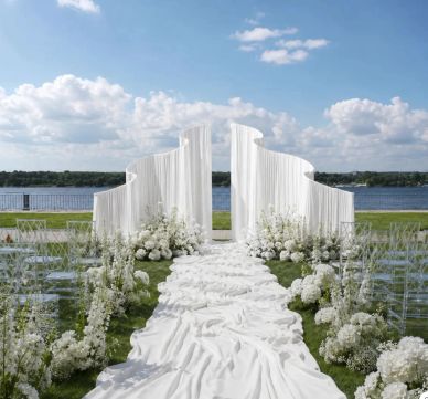 Elegant outdoor wedding setup with white decorations by the water.