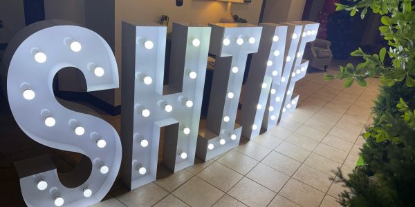 Large illuminated SHINE letters indoors.