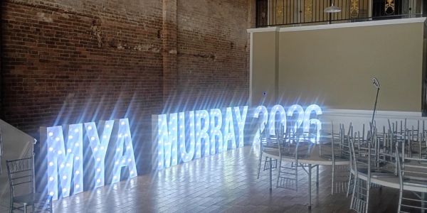 Illuminated letters spelling 'MYA MURRAY 2026' in a room.