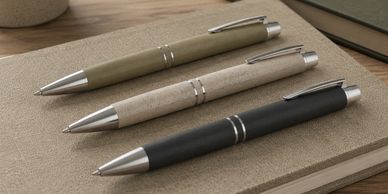 Three elegant pens in earth tones placed on a textured notebook.