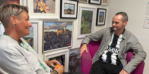 Two people talking in a room with framed photos.