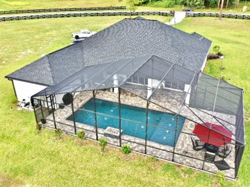 House with screened-in pool and patio area with umbrella and chairs.