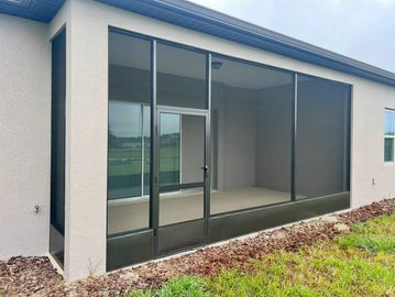 A screened-in porch attached to a modern house with a grass and mulch border.
