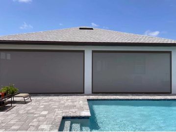 Covered patio windows behind a pool with clear blue skies.