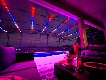 Cozy poolside seating area illuminated with vibrant red, blue, and purple lights at night.