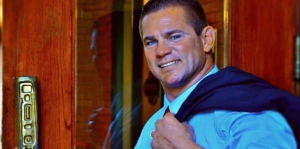 Man in blue shirt holding a door handle and jacket over shoulder.