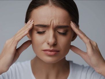 Young woman with eyes closed holding temples in pain.