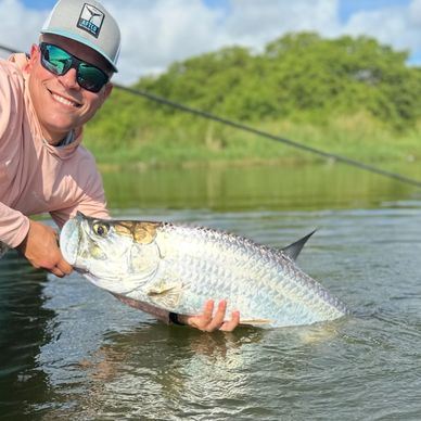 Hombre con gran pez plateado en el agua.