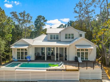 Modern white house with a pool and spacious deck surrounded by trees.
