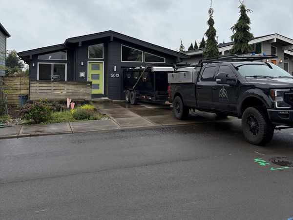Modern black house with a bright green door and a black truck parked outside on a rainy day.