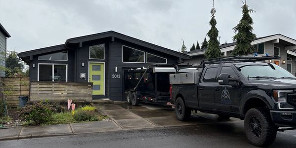 Black truck parked in front of modern dark-gray house with green door.