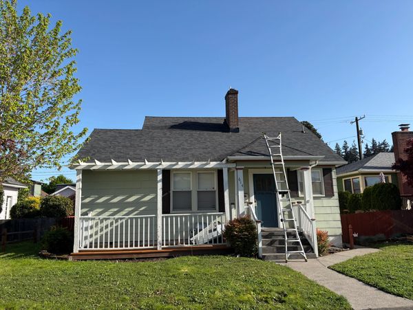 Small house with a ladder leaning on the front porch under a clear blue sky.
