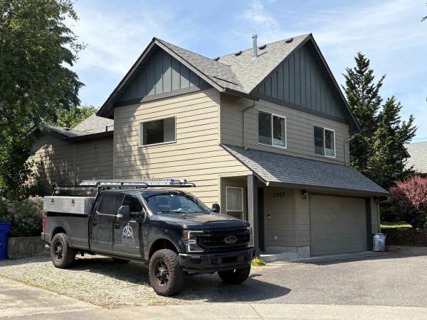 A black utility truck parked beside a two-story modern house on a sunny day.