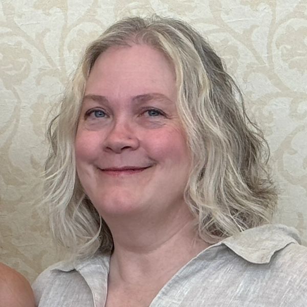 A smiling woman with shoulder-length blonde hair in a light-colored shirt.