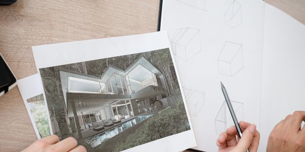 Manos diseñando un plano arquitectónico con impresión de casa moderna.