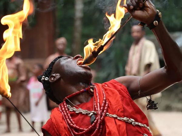 A performer dressed in red executes a fire-eating act, surrounded by onlookers.