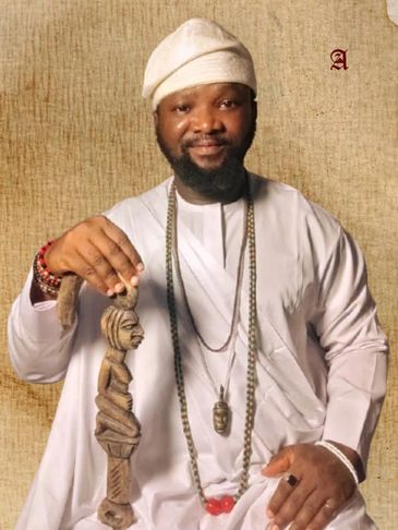 Man in traditional attire holding a carved wooden sculpture.